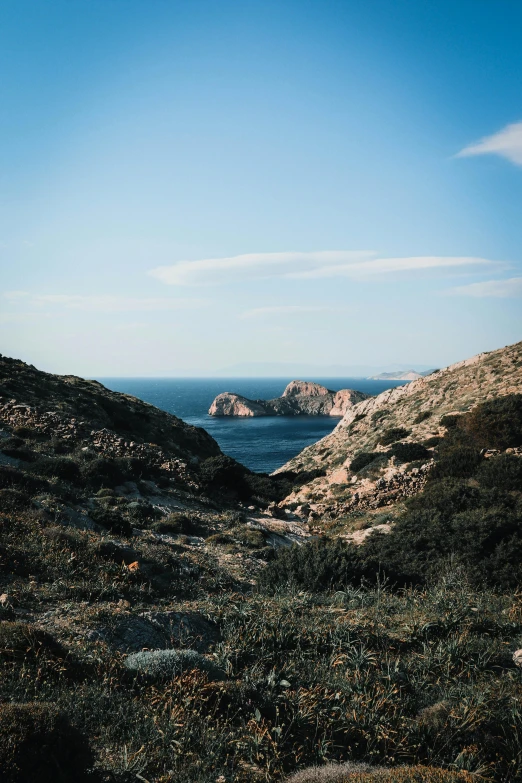 a man standing on top of a hill next to a body of water, by Alexis Grimou, les nabis, calanque, view from a distance, slightly tanned, rocky grass field