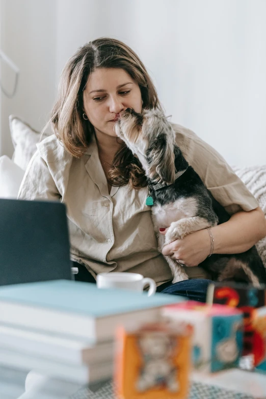 a woman sitting on a couch with a dog and a laptop, kissing each other, supportive, snacks, on a desk