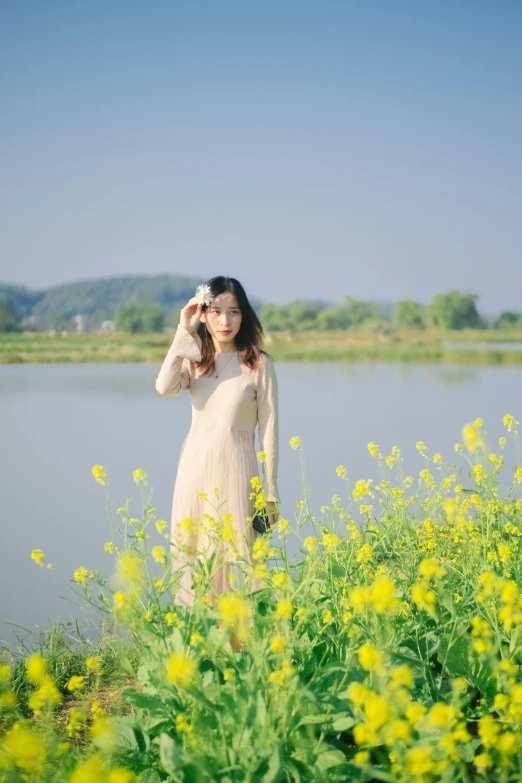 a woman standing in a field of yellow flowers, a picture, by Tan Ting-pho, romanticism, beside the river, low quality photo, 奈良美智, 8k 28mm cinematic photo