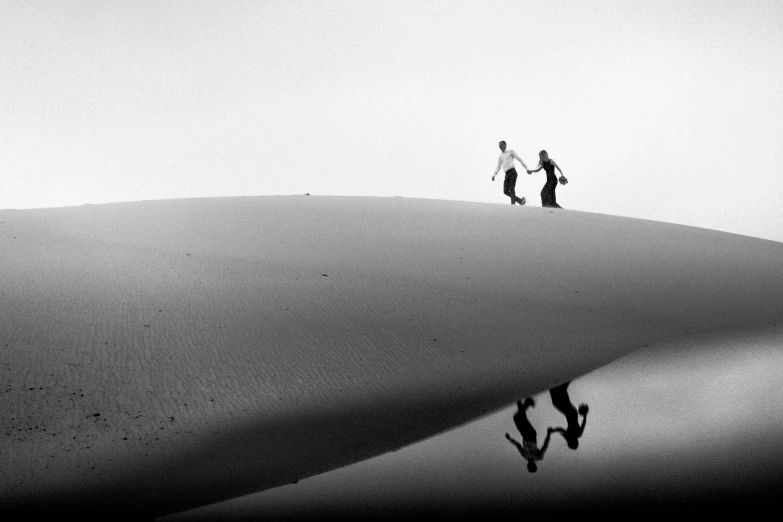 a black and white photo of two people walking on a hill, by Ibrahim Kodra, unsplash contest winner, minimalism, couple dancing, sand banks, beautiful reflexions, indonesia national geographic