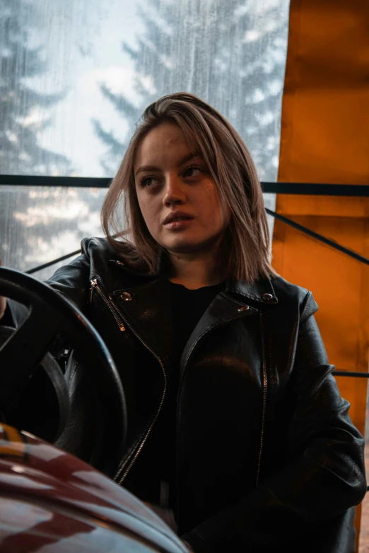 a woman sitting in the driver's seat of a car, inspired by Elsa Bleda, pexels contest winner, wearing a black leather jacket, joey king, black and orange, 🤤 girl portrait