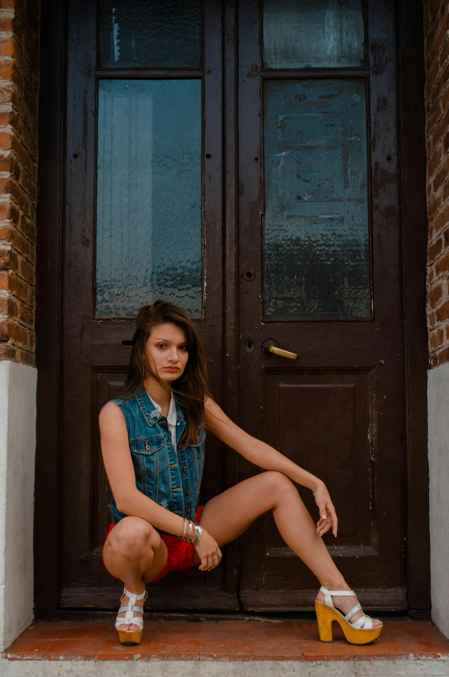 a woman sitting on a step in front of a door, a portrait, by Sven Erixson, pexels contest winner, daisy dukes, russian style, low quality photo, in shorts