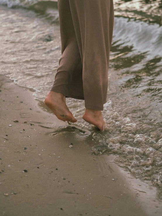 a person walking on a beach next to the ocean, exposed toes, muted browns, emerging from the water, promo image