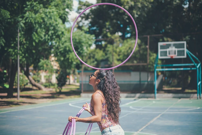 a woman standing on top of a tennis court holding a hoop, by Gina Pellón, pexels contest winner, purple tubes, at a park, justina blakeney, vanessa morgan