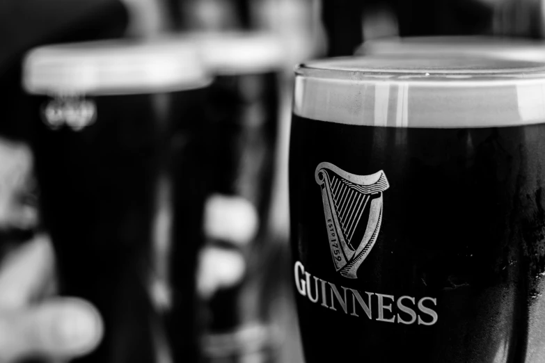 a close up of a glass of beer on a table, a black and white photo, by Carey Morris, pexels, pots of gold, dressed in black, ireland, in a row
