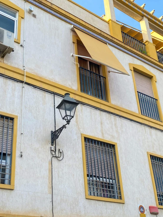 a yellow and white building with a blue sky in the background, inspired by Luis Paret y Alcazar, unsplash, one single gas lamp, awnings, square, low quality photo