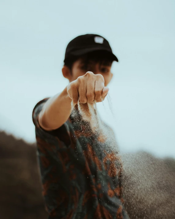 a person that is throwing sand in the air, by Robbie Trevino, fighting stance, lgbtq, hand holding cap brim, cleanest image