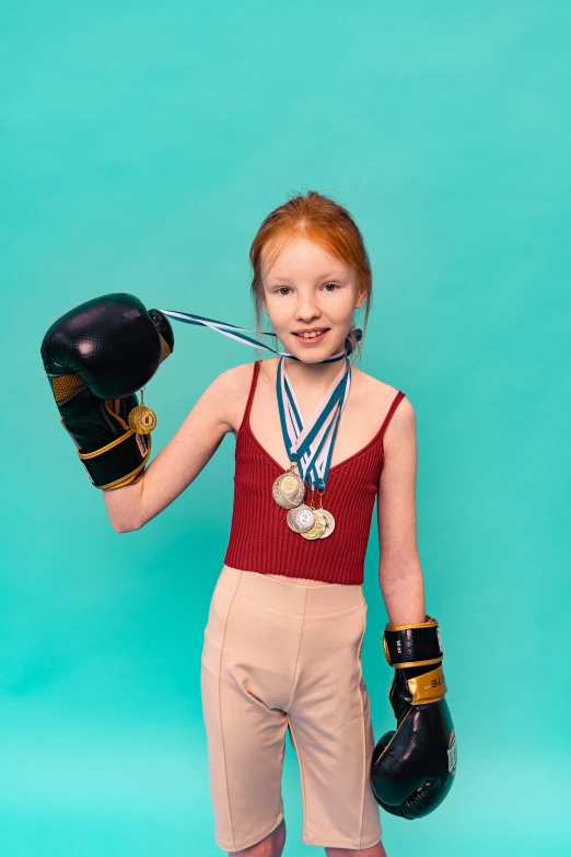 a young girl holding a pair of boxing gloves, by Ellen Gallagher, pexels contest winner, pop art, ginger hair with freckles, wax figure, gold belt, wearing track and field suit