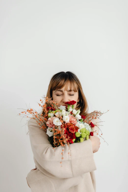 a woman holding a bunch of flowers in front of her face, white and red color scheme, giggling, head bowed slightly, white and orange