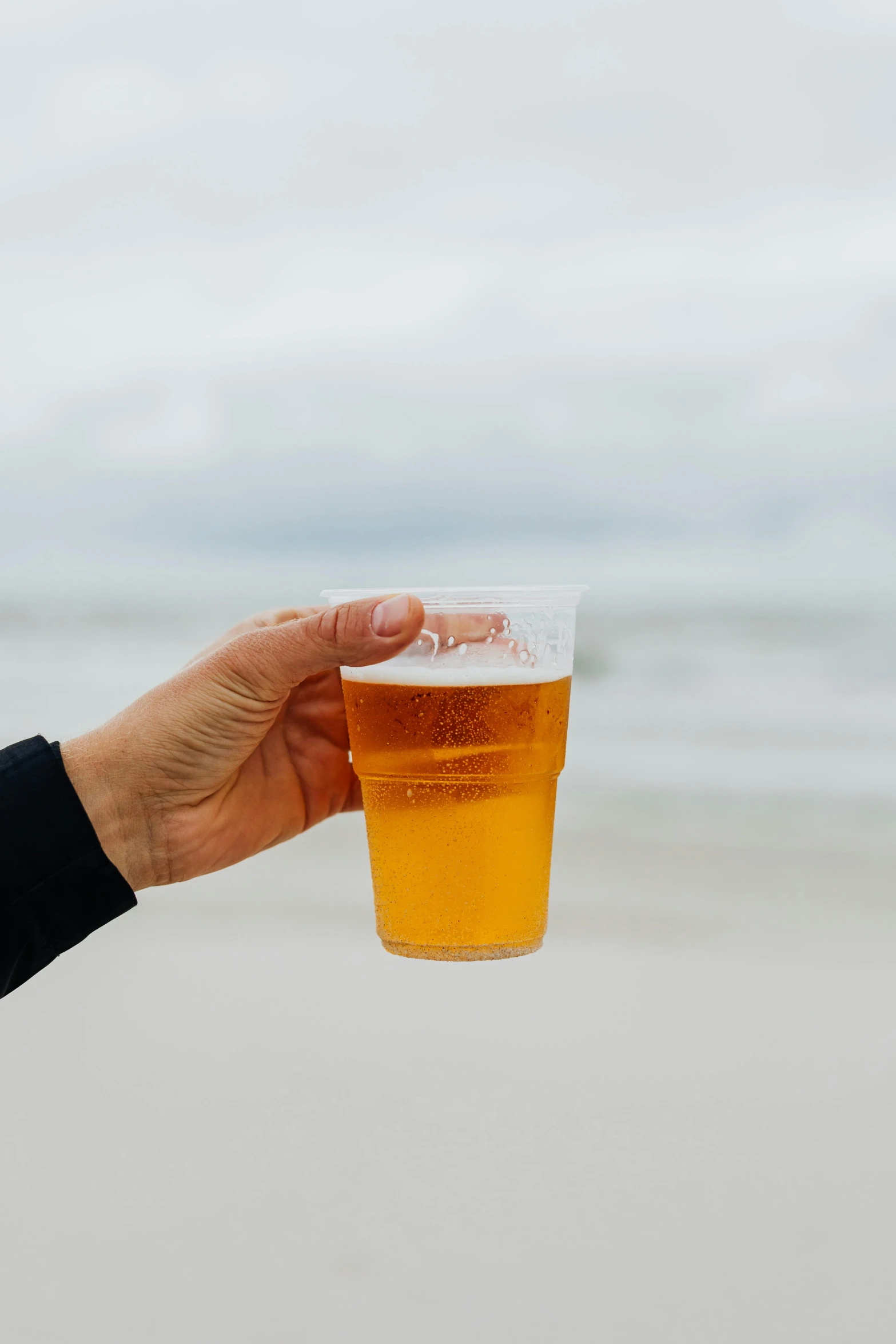 a person holding a glass of beer on the beach, no - text no - logo, college, paper, slight overcast