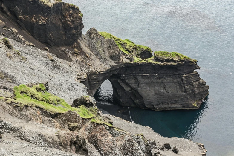 a man standing on top of a cliff next to a body of water, by Hallsteinn Sigurðsson, pexels contest winner, hurufiyya, massive arch, close-up from above, structural geology, 2 0 0 0's photo