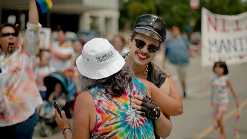 a couple of women standing next to each other on a street, a photo, trending on reddit, wearing a bandana and chain, pride parade, picture of a male biker, wearing a white bathing cap