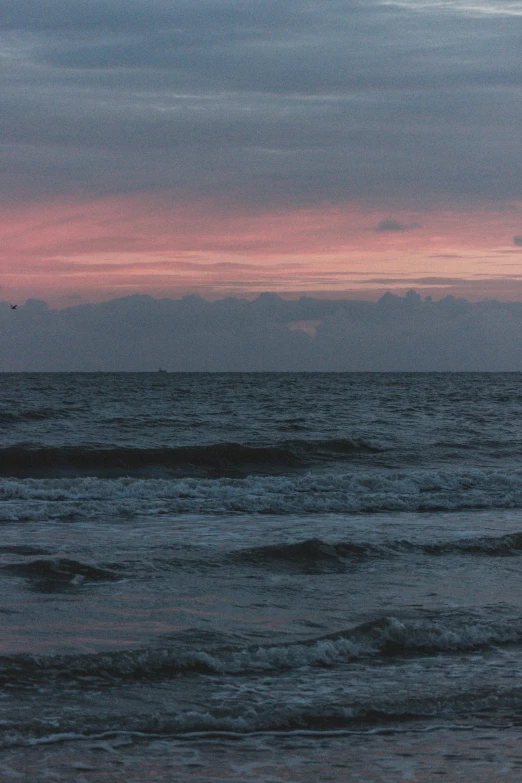 a person flying a kite on top of a beach, pink clouds in the sky, rough waters, february)