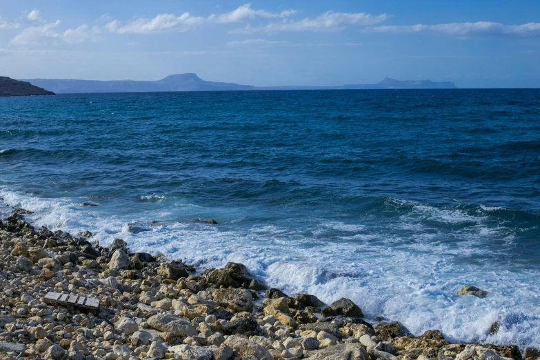 a large body of water sitting on top of a rocky beach, a picture, by Simon Marmion, unsplash, greeks, rough seas in background, blue, slide show