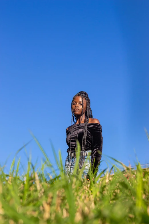 a woman standing on top of a lush green field, an album cover, trending on pexels, black teenage girl, clear blue sky, portrait shot 8 k, color ( sony a 7 r iv