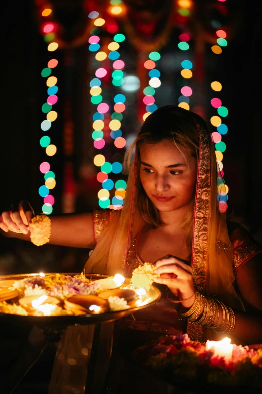 a woman sitting at a table with a plate of food in front of her, floating lanterns, hindu ornaments, leds, a girl with blonde hair