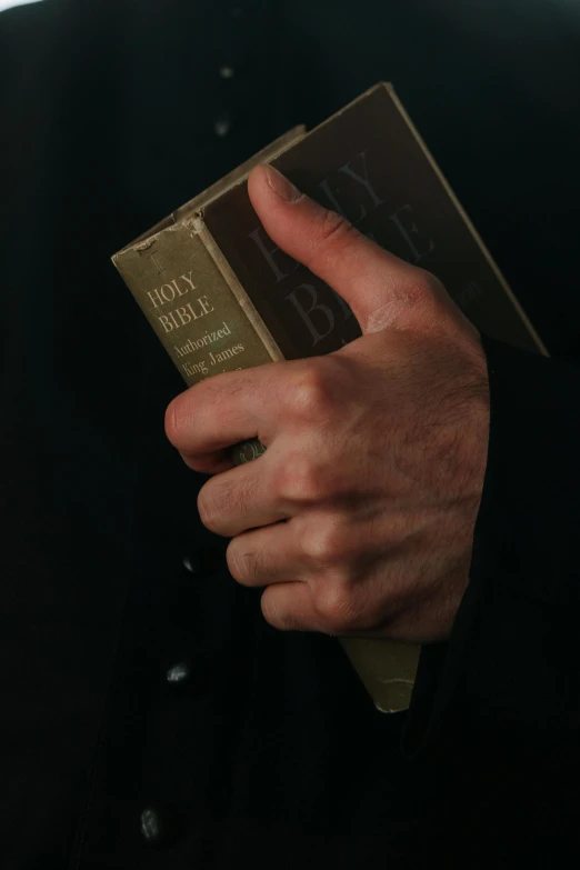 a close up of a person holding a book, finger of god, man in black, 1960s color photograph, 15081959 21121991 01012000 4k