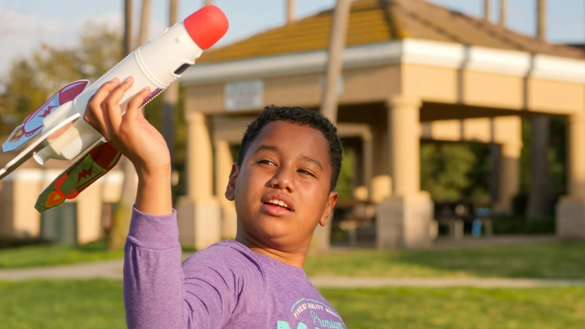 a young boy holding a toy airplane in his hand, by Michael Goldberg, pexels contest winner, prosthetic arm, at a park, holding a rocket launcher, avatar image