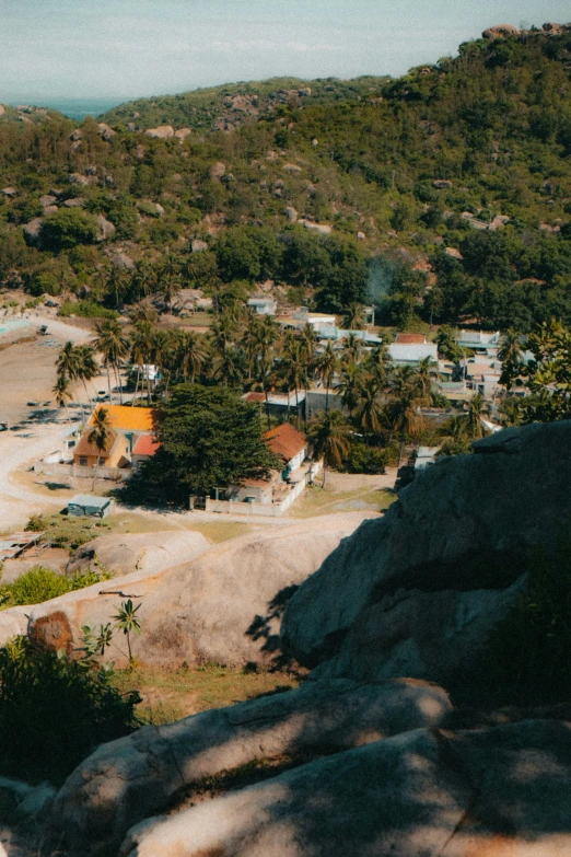 a view of a beach from the top of a hill, small buildings, jungle setting, aerial view cinestill 800t 18mm, rocky hills