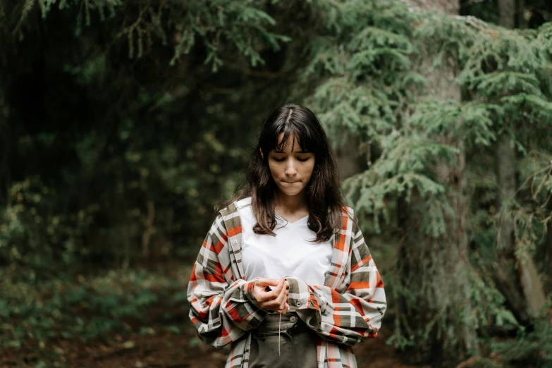 a woman standing in the woods looking at her cell phone, a portrait, by Emma Andijewska, pexels contest winner, plaid shirt, madison beer as leeloo, slightly minimal, forest ritual