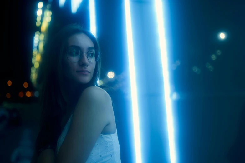 a woman wearing glasses standing in front of neon lights, inspired by Elsa Bleda, pexels contest winner, dramatic white and blue lighting, medium format. soft light, young woman in her 20s, portrait mode photo