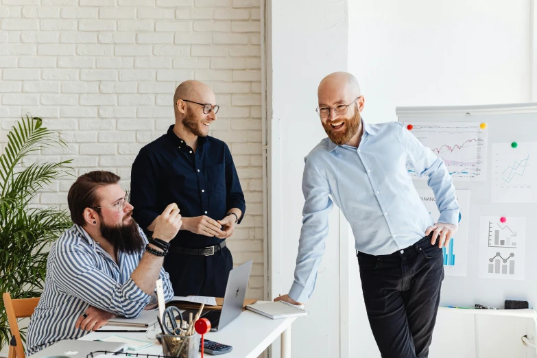 a group of men standing around a table, pexels contest winner, it specialist, smiling at each other, office clothes, bending down slightly