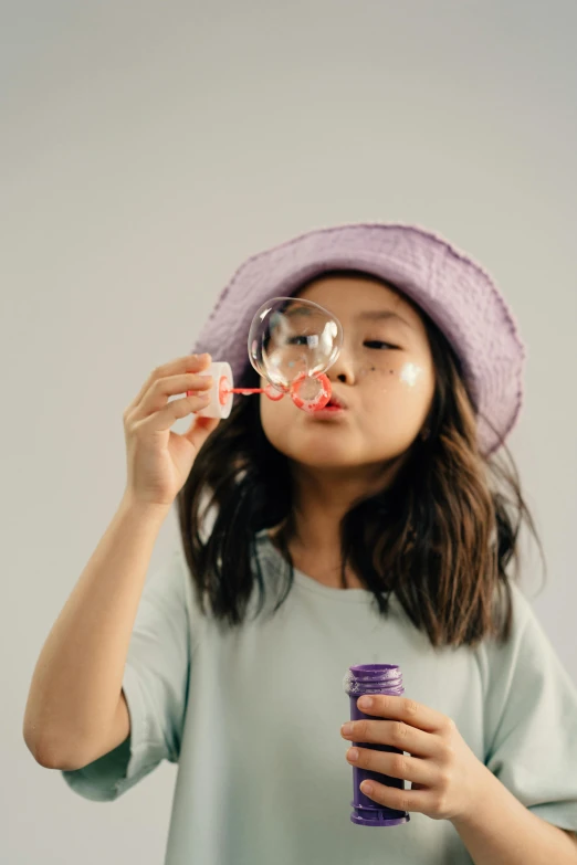 a girl in a purple hat blowing bubbles, pexels contest winner, set against a white background, taejune kim, toy commercial photo, on grey background