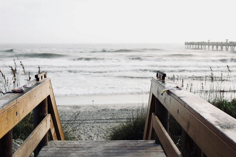 a wooden walkway leading to a beach next to the ocean, a picture, by Carey Morris, unsplash, ((waves, a cozy, steps, background image