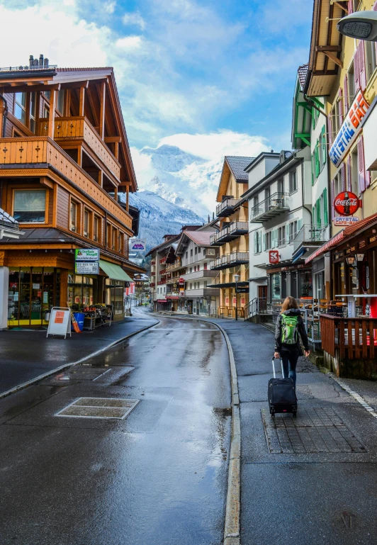 a person with a suitcase walking down a street, inspired by Karl Stauffer-Bern, pexels contest winner, lauterbrunnen valley, square, skiing, shops