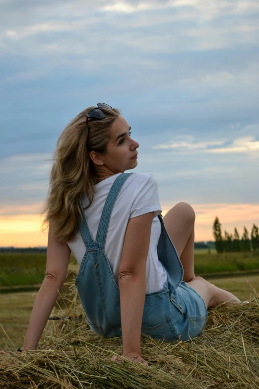 a woman sitting on top of a pile of hay, pexels contest winner, wearing overalls, profile image, wearing : tanktop, summer evening