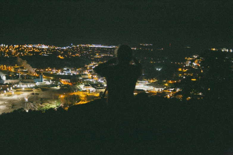 a person standing on top of a hill at night, surrounding the city, nightlife, facing away from the camera, from afar