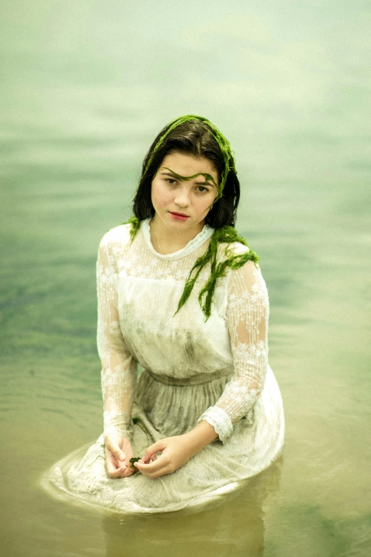 a woman in a white dress sitting in the water, an album cover, inspired by Elsa Bleda, renaissance, green clothes, maisie williams, weathered olive skin, looking towards camera