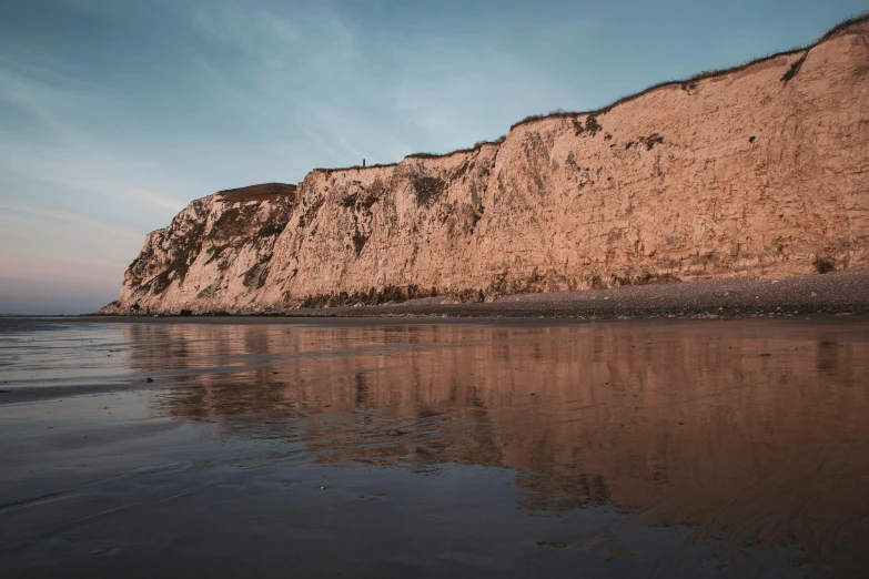 a man riding a surfboard on top of a sandy beach, by Thomas Furlong, unsplash contest winner, hyperrealism, chalk cliffs above, cliff side at dusk, hollister ranch, half submerged in heavy sand