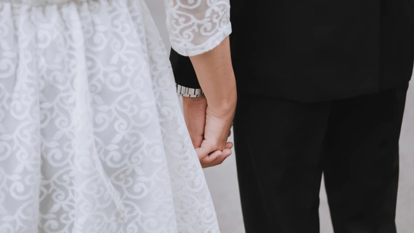 a close up of a bride and groom holding hands, white and black clothing, promo image, background image, unedited