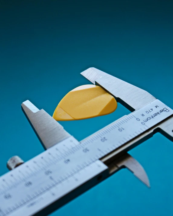 a close up of a caliper on a blue background, by Doug Ohlson, plasticien, gradient yellow, measurements, guitar shape build, thumbnail