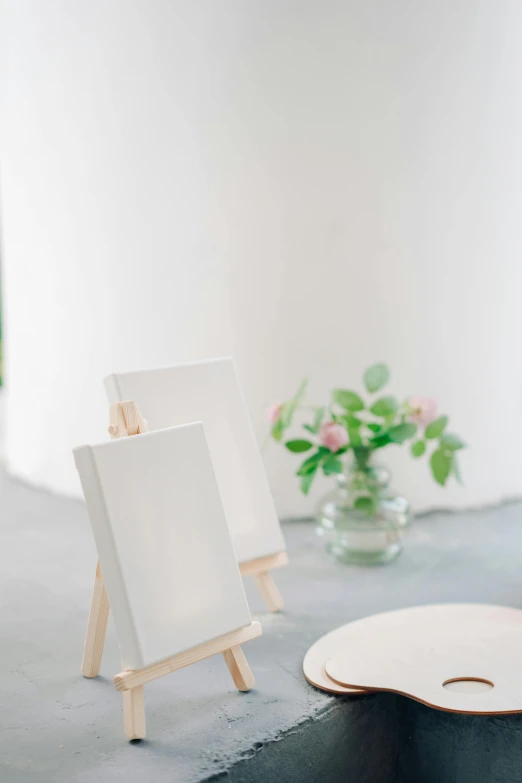 a couple of easels sitting on top of a table, a minimalist painting, inspired by Constantin Hansen, unsplash, visual art, wedding, books and flowers, overexposed photograph, smooth tiny details