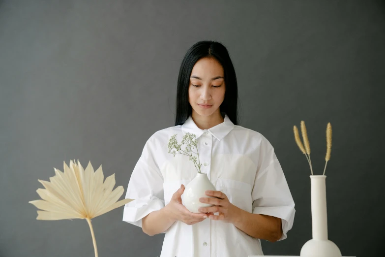 a woman in a white shirt holding a white vase, inspired by Kim Tschang Yeul, pexels contest winner, lab coat and tee shirt, white petal, from side, botanical