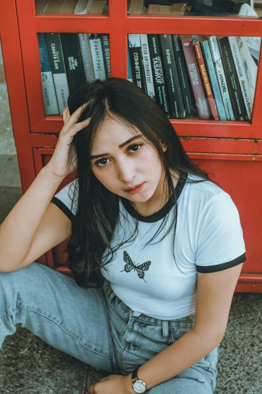 a woman sitting on the floor in front of a bookshelf, an album cover, inspired by Ni Yuanlu, trending on pexels, wearing a t-shirt, girl cute-fine-face, indonesia, headshot profile picture
