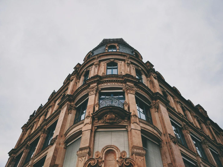a tall building with a clock on the front of it, a photo, unsplash contest winner, art nouveau, muted browns, overcast skies, looking up at camera, fancy apartment