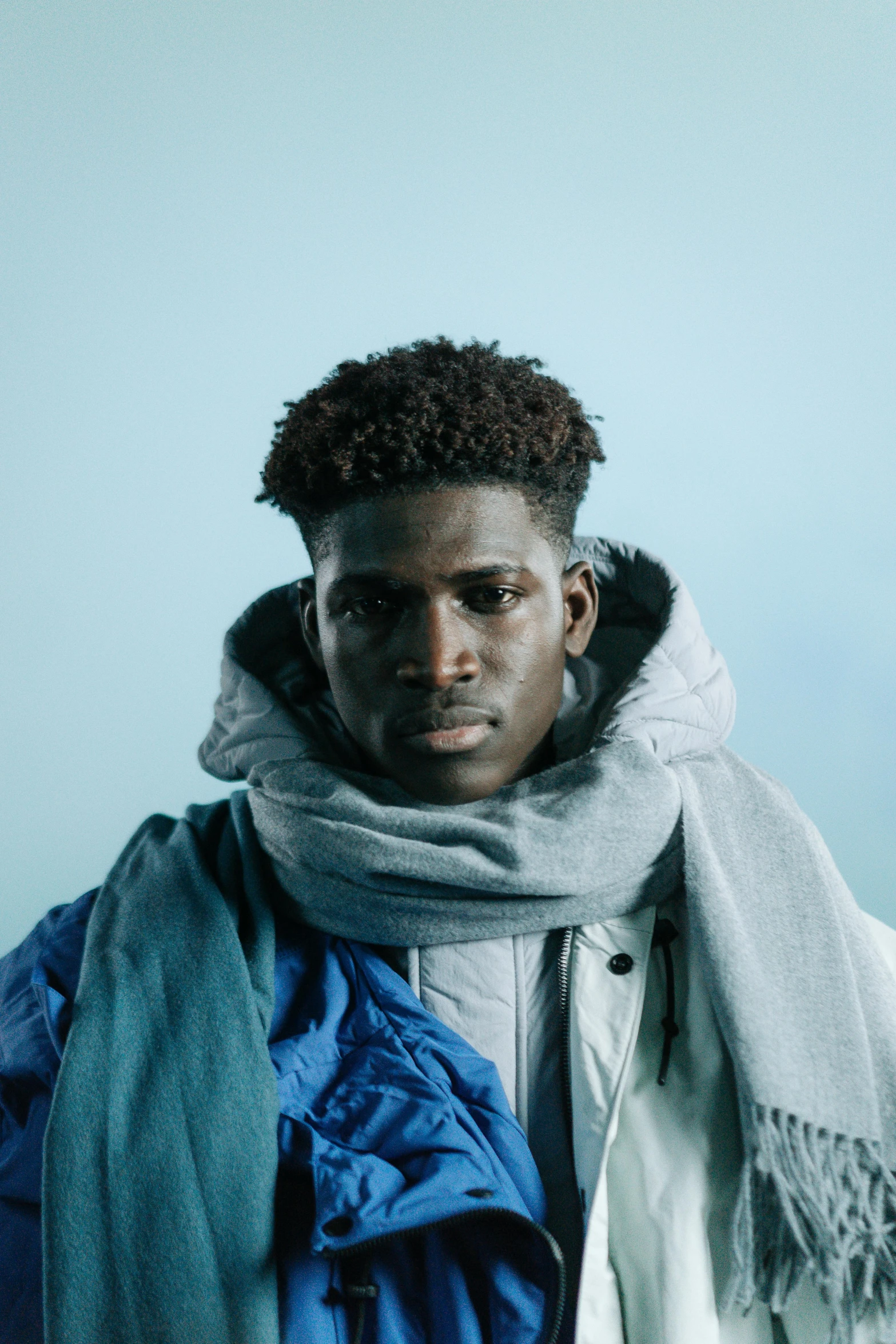 a man with a scarf around his neck, inspired by Paul Georges, trending on unsplash, model wears a puffer jacket, black teenage boy, blue - grey gear, studio photo