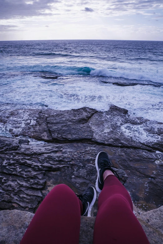 a person sitting on top of a rock next to the ocean, happening, manly, lots of swirling, feet on the ground, 6 : 3 0 am