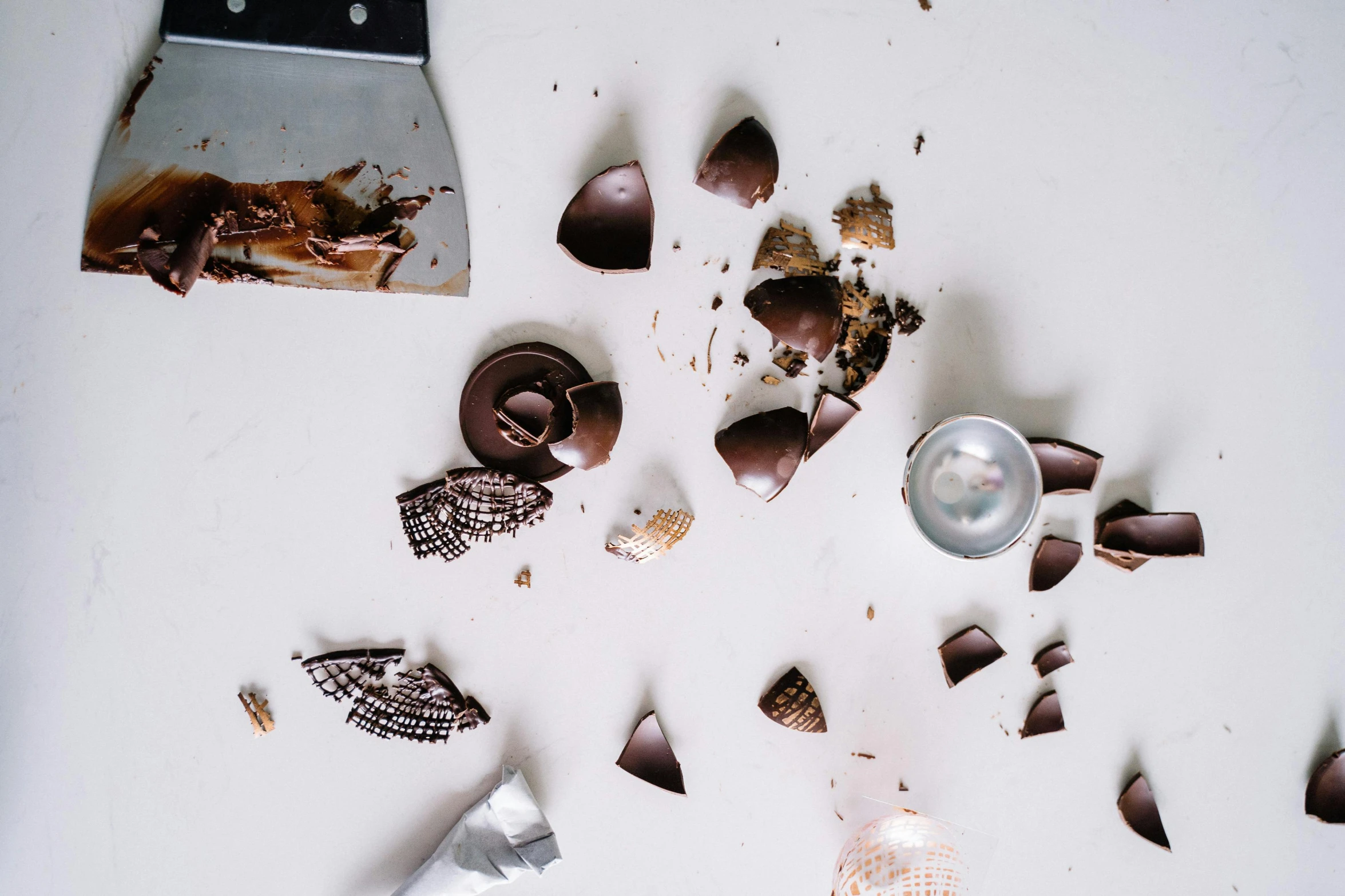 a couple of pieces of chocolate sitting on top of a table, trending on pexels, assemblage, debris flying around, spoon placed, shells, on a white table