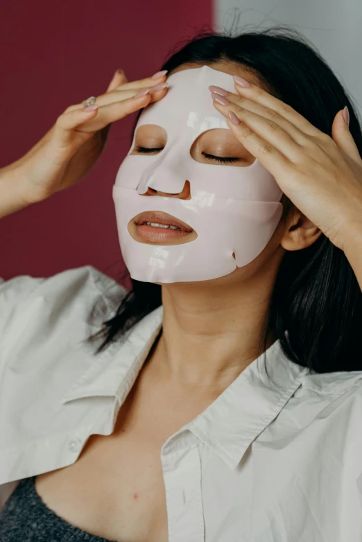 a woman putting a mask on her face, an album cover, trending on pexels, silicone skin, asian female, relaxed expression, face and body