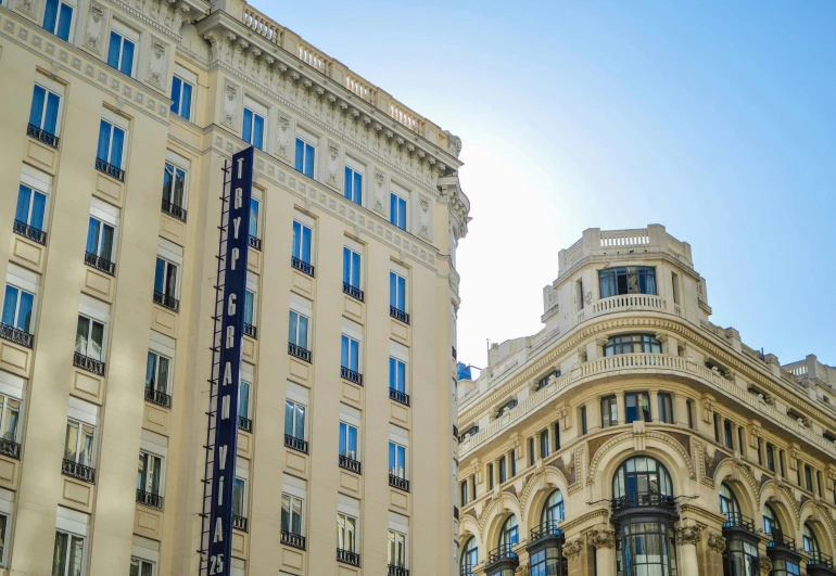 a couple of tall buildings next to each other, inspired by Tomàs Barceló, unsplash, art nouveau, madrid, square, clear blue skies, bulgari