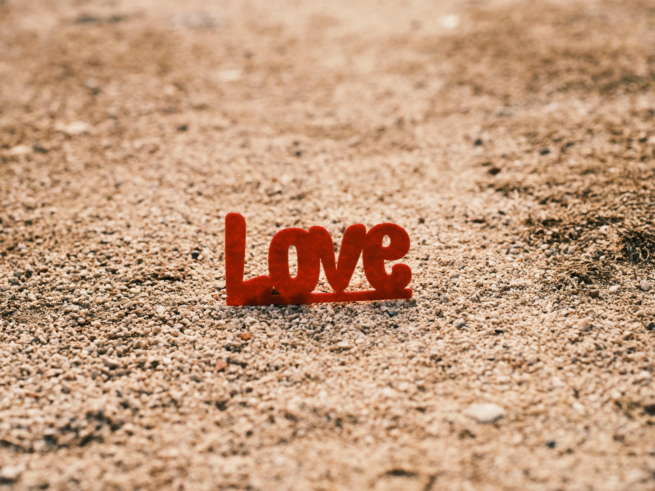 a red love sign sitting on top of a sandy beach, unsplash, graffiti, background image, miniature product photo, red dusty soil, profile picture