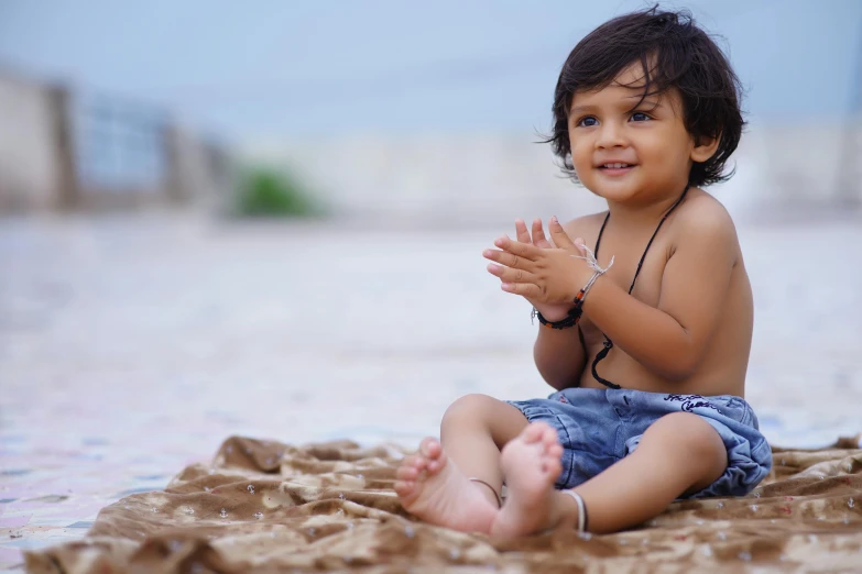 a small child sitting on top of a sandy beach, by Thota Vaikuntham, pexels contest winner, hurufiyya, cute young man, welcoming attitude, tummy, subtle detailing