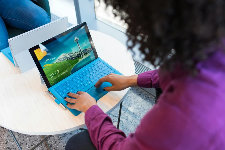 a woman sitting at a table using a laptop computer, by Meredith Dillman, unsplash, happening, microsoft windows, blue themed, using a magical tablet, slide show