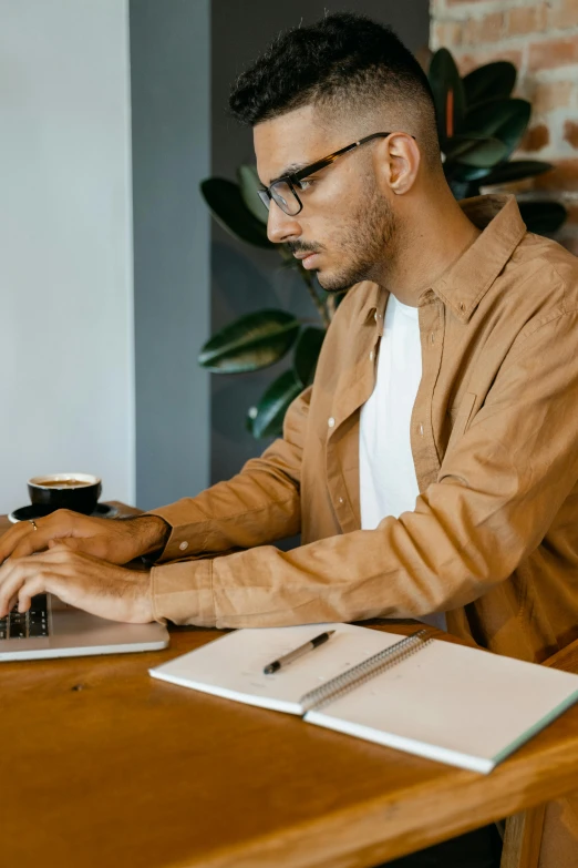 a man sitting at a table working on a laptop, trending on pexels, arbeitsrat für kunst, brown, non-binary, serious expression, thumbnail