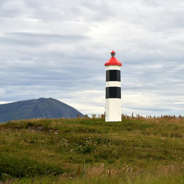 a lighthouse sitting on top of a lush green hillside, by Hallsteinn Sigurðsson, hurufiyya, it has a red and black paint, taken in the early 2020s, brochure, monument