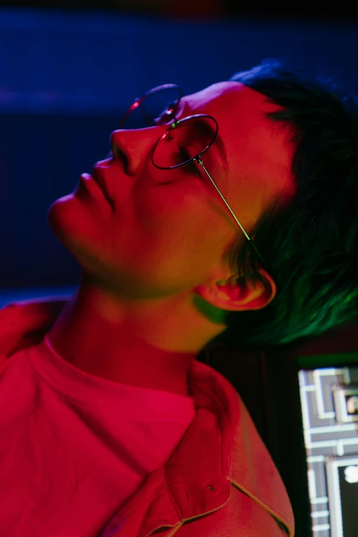 a man with green hair sitting in front of a computer, an album cover, inspired by Liam Wong, trending on pexels, holography, wearing red tainted glasses, bisexual lighting, close-up portrait film still, as she looks up at the ceiling